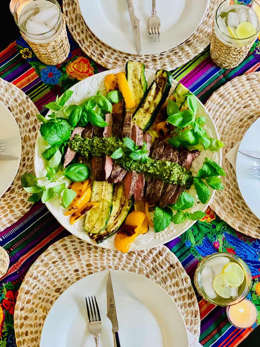 A table set for a summer barbecue, featuring grilled steaks and chimichurri sauce