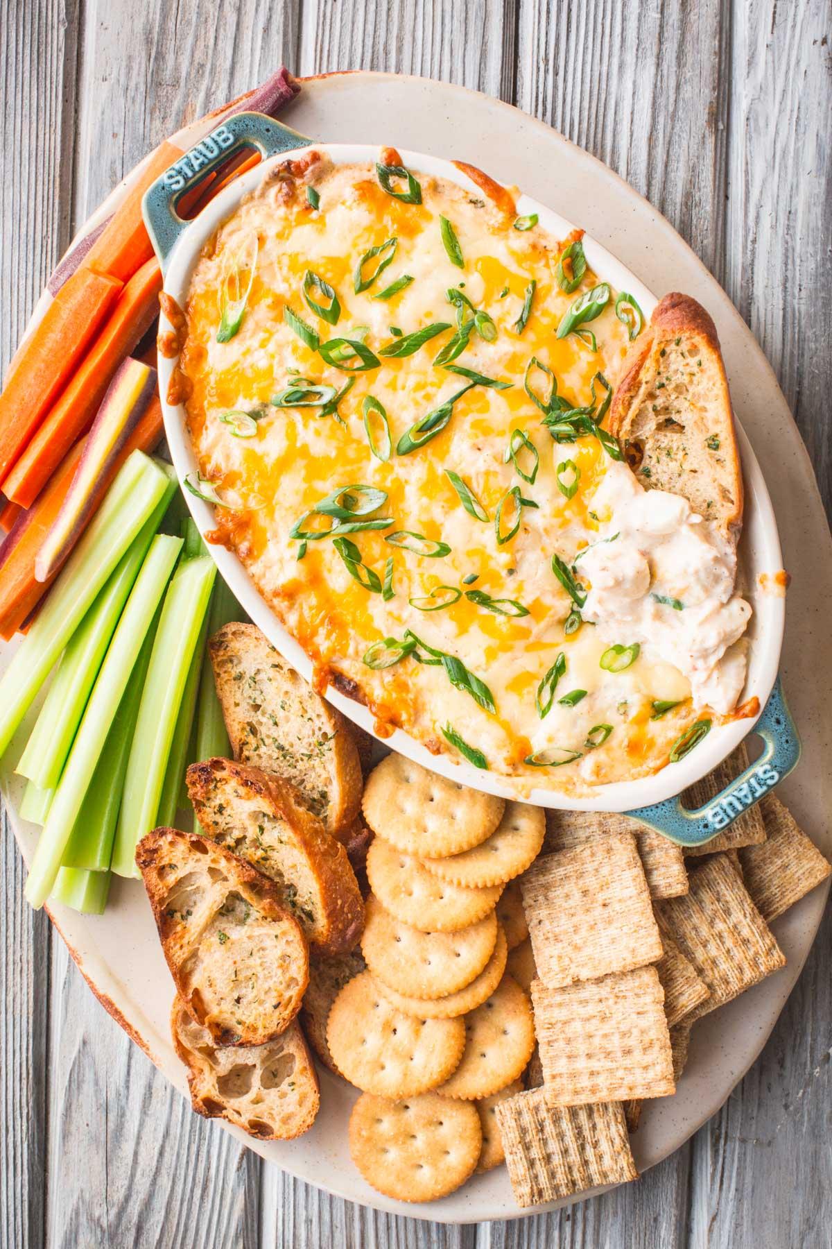 baked crab dip on a serving platter with various dippers like crackers, bread, and vegetable sticks