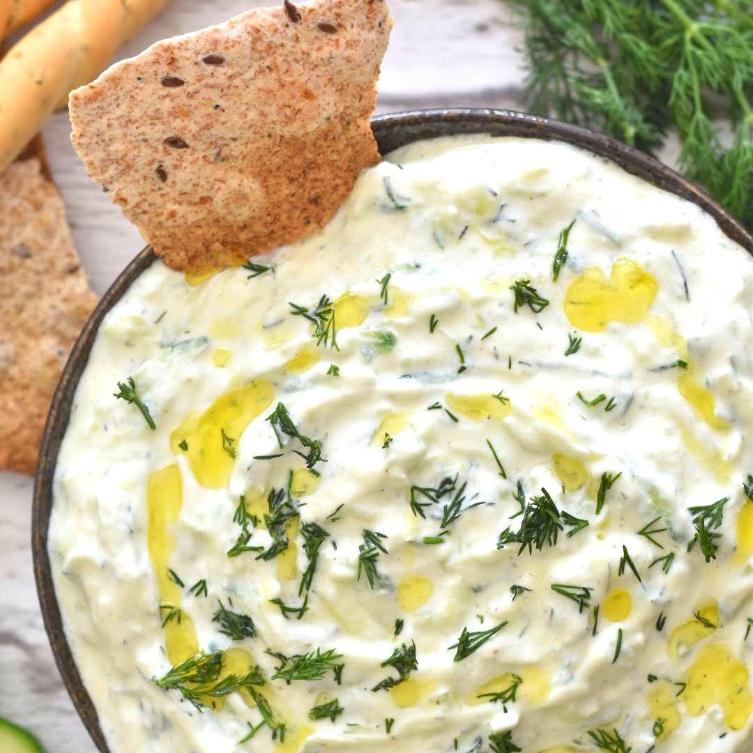 Close-up shot of creamy cucumber-dill tzatziki in a white bowl, garnished with fresh dill and a sprinkle of paprika