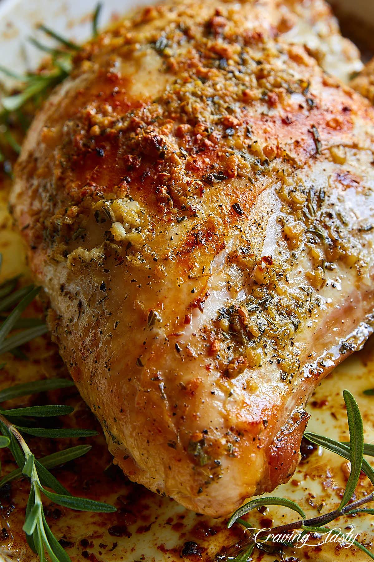 Close-up of a raw turkey breast being coated with a peppercorn and herb rub
