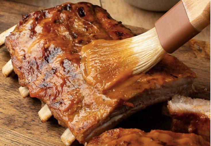 A close-up of the ribs being basted with mango BBQ sauce on the smoker.