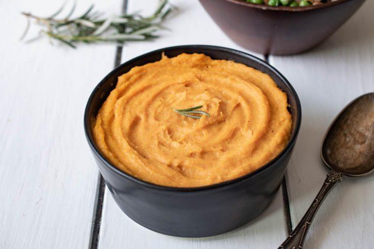 Close-up shot of a bowl of creamy roasted carrot and parsnip puree, garnished with fresh herbs