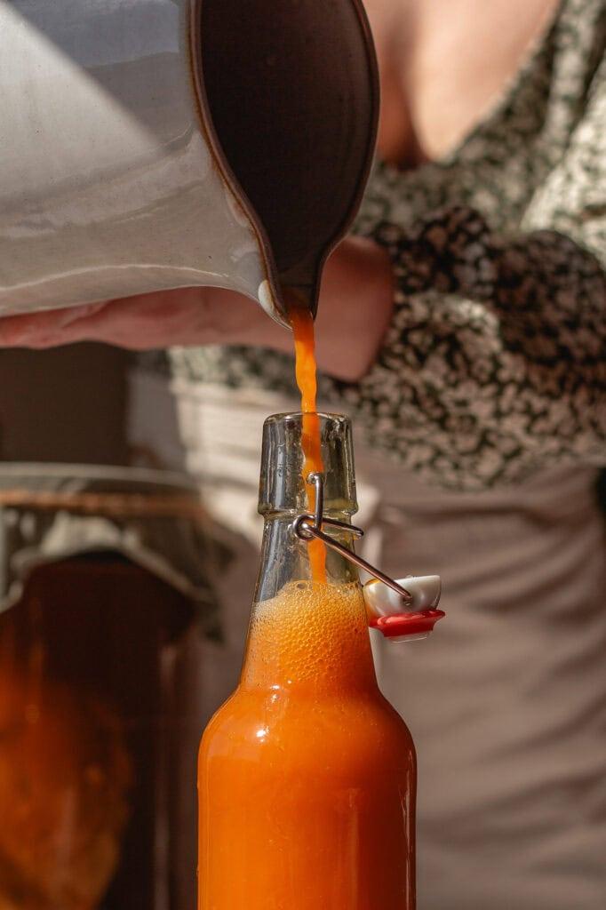 Close-up shot of a person pouring blood orange kombucha into a glass