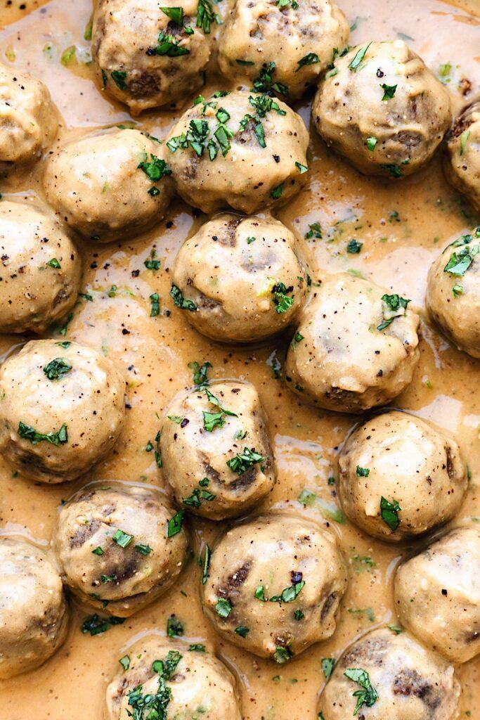 Close up of a single plant based meatball covered in creamy cheese sauce