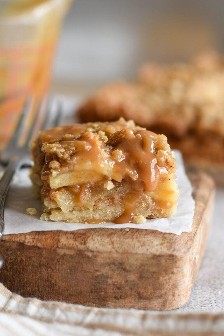 Caramel apple bars with a drizzle of caramel on a wooden surface