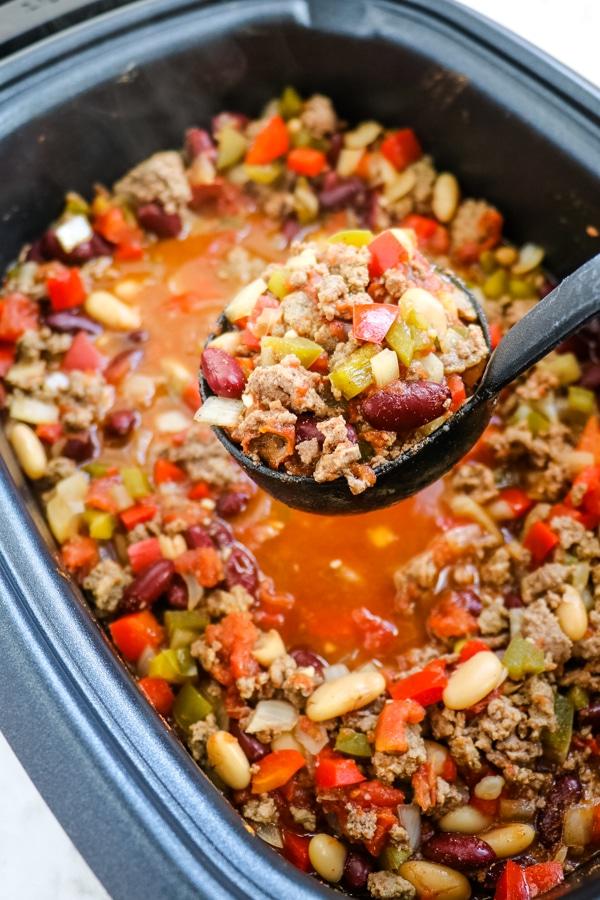 A person ladling chili from a slow cooker into bowls