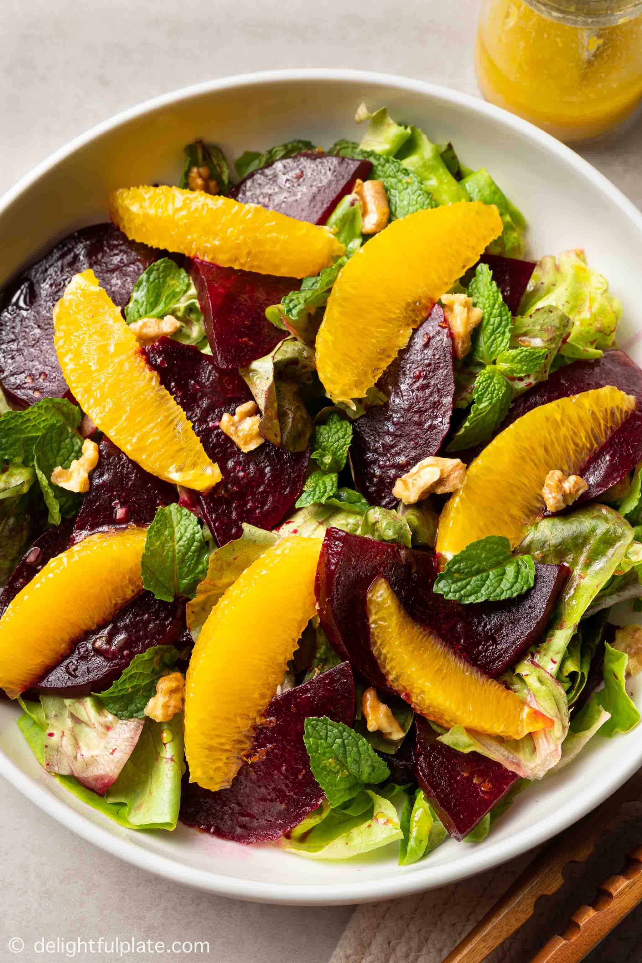 Hands arranging roasted beet slices on a plate with fresh greens