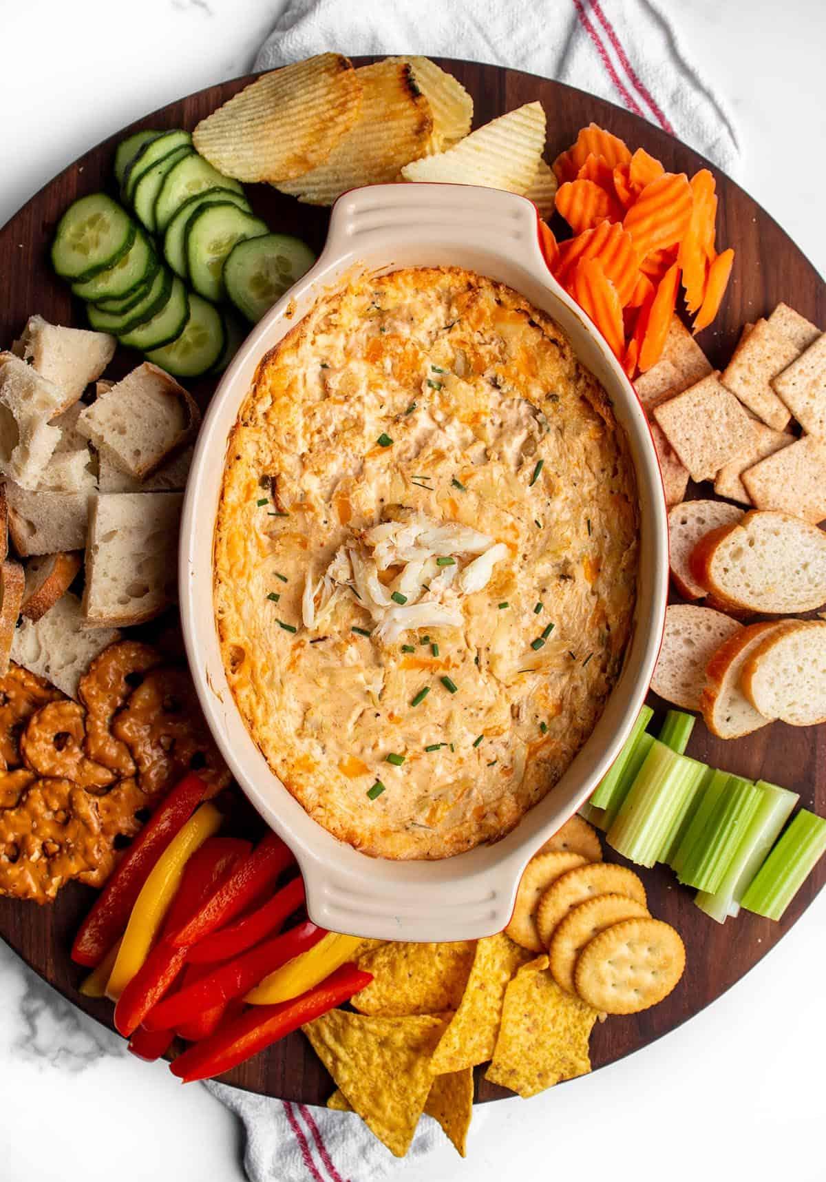 overhead shot of a baked crab dip platter with various dippers like crackers, bread, and vegetables, ready for a party