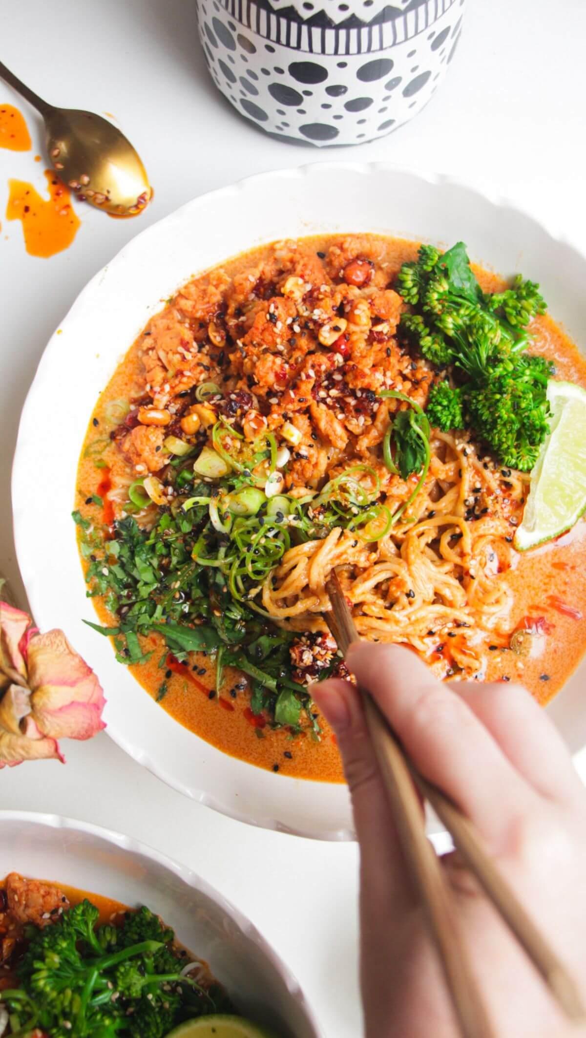 hands mixing peanut noodles with chicken and rice in a bowl