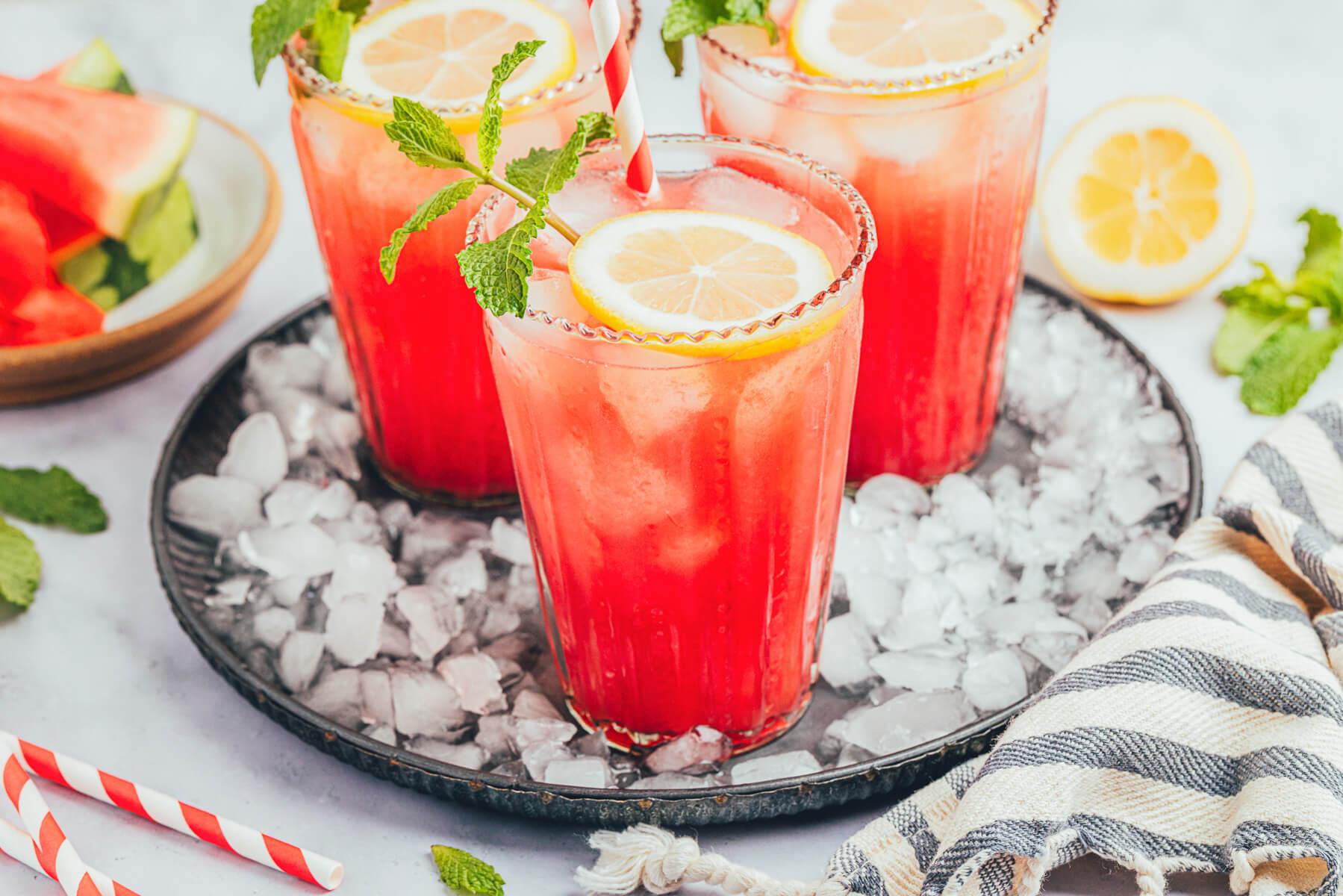 pitcher of watermelon thyme lemonade surrounded by fresh watermelons, lemons, and thyme sprigs