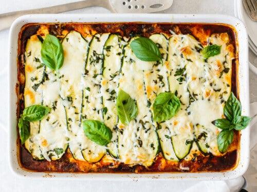 Baked zucchini lasagna with melted cheese, parsley garnish, and served in a baking dish
