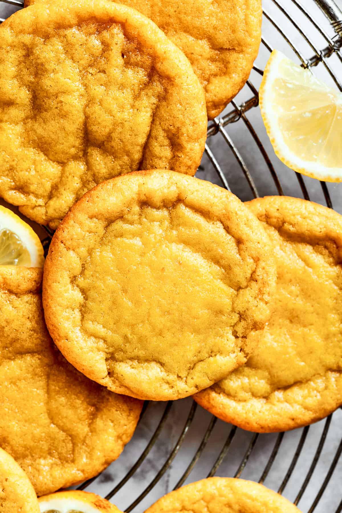 Close-up of golden lemon cookies with bright yellow zest sprinkled on top, on a cooling rack, sunlight streaming in