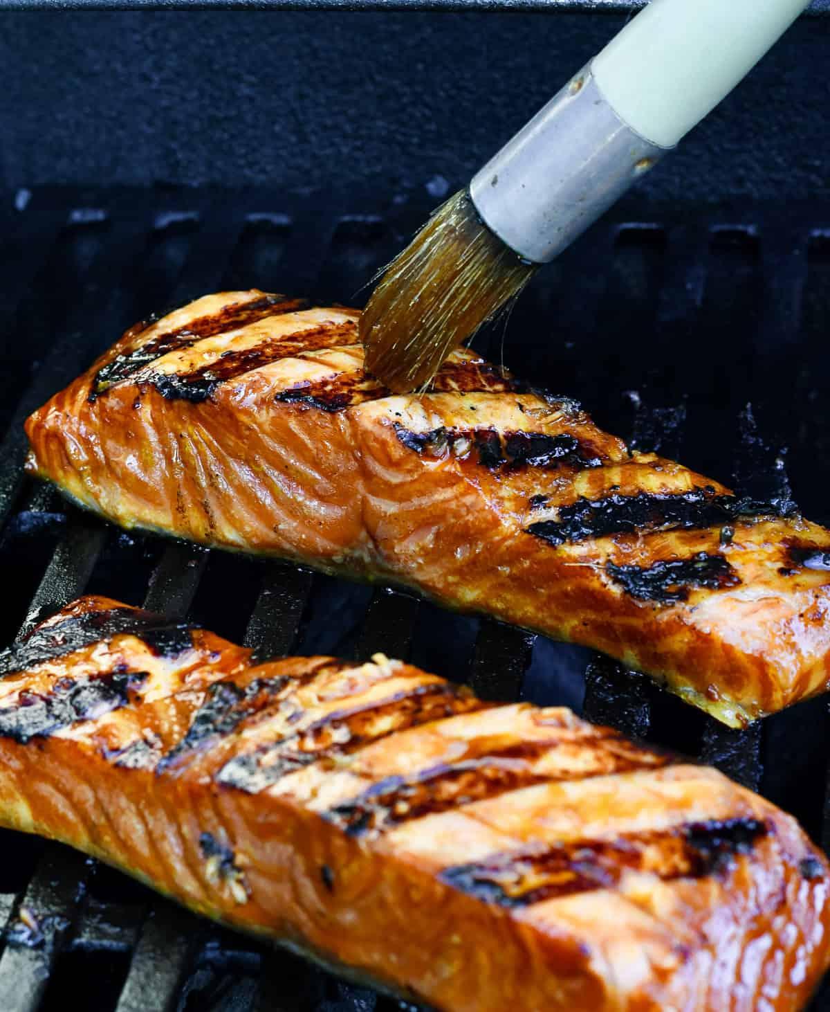 close up of a chef brushing honey glaze onto salmon on the grill