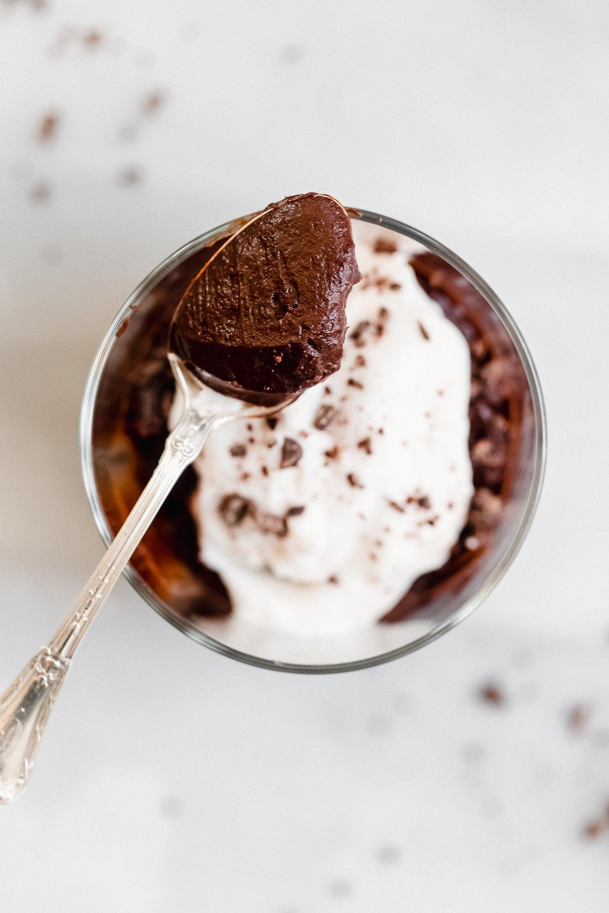 A close-up shot of a spoonful of avocado chocolate mousse being lifted, showing its creamy texture.