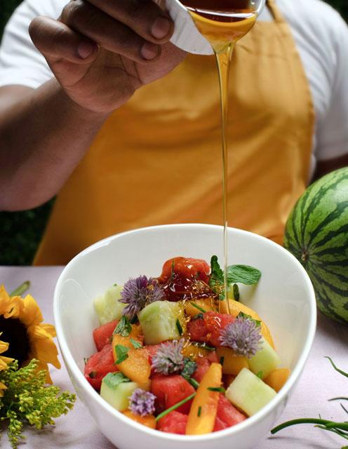 a hand tossing watermelon peach and mint salad in large bowl
