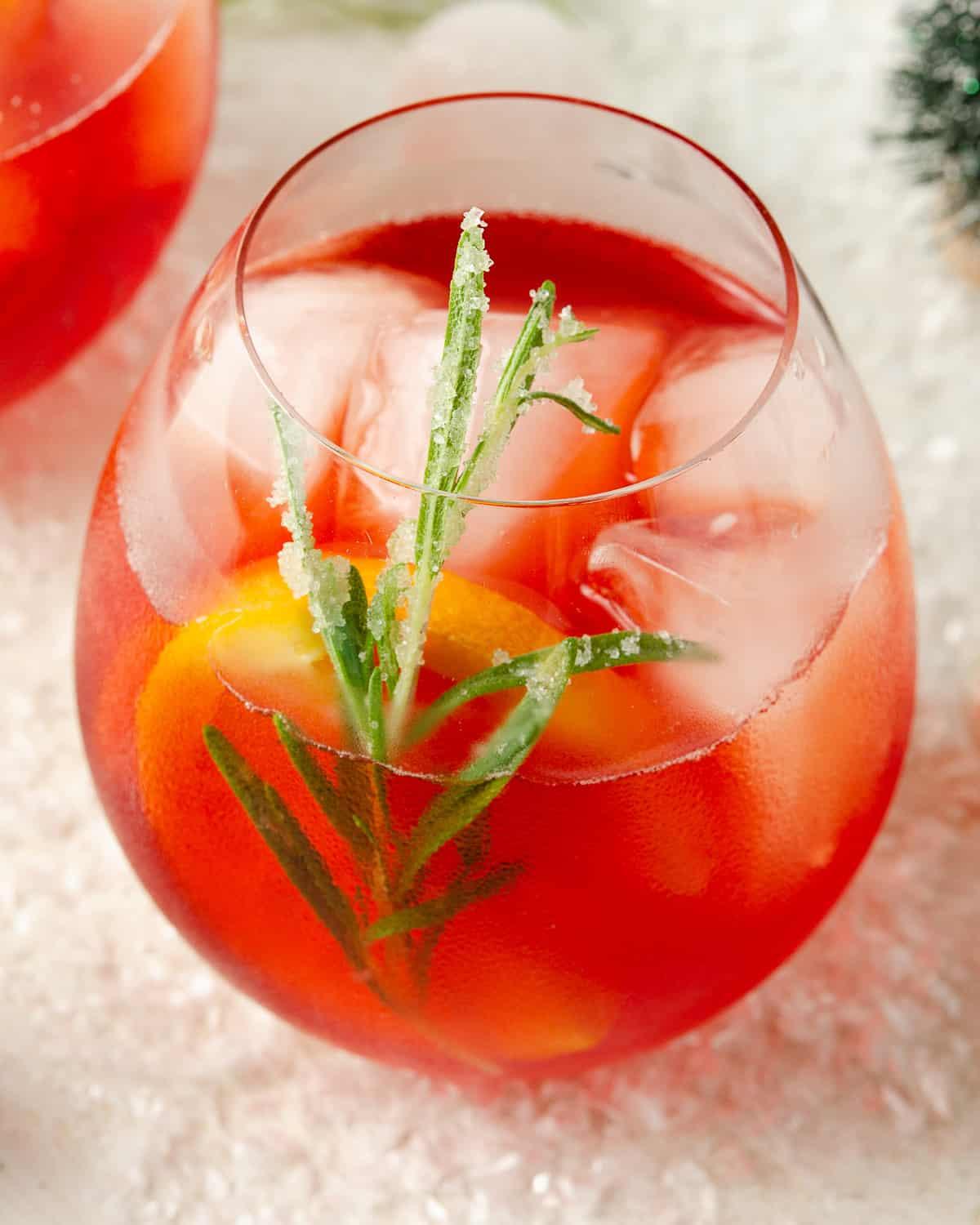 Close-up of a sparkling cranberry spritz with ice, rosemary, and orange slice garnish, bright and refreshing feel