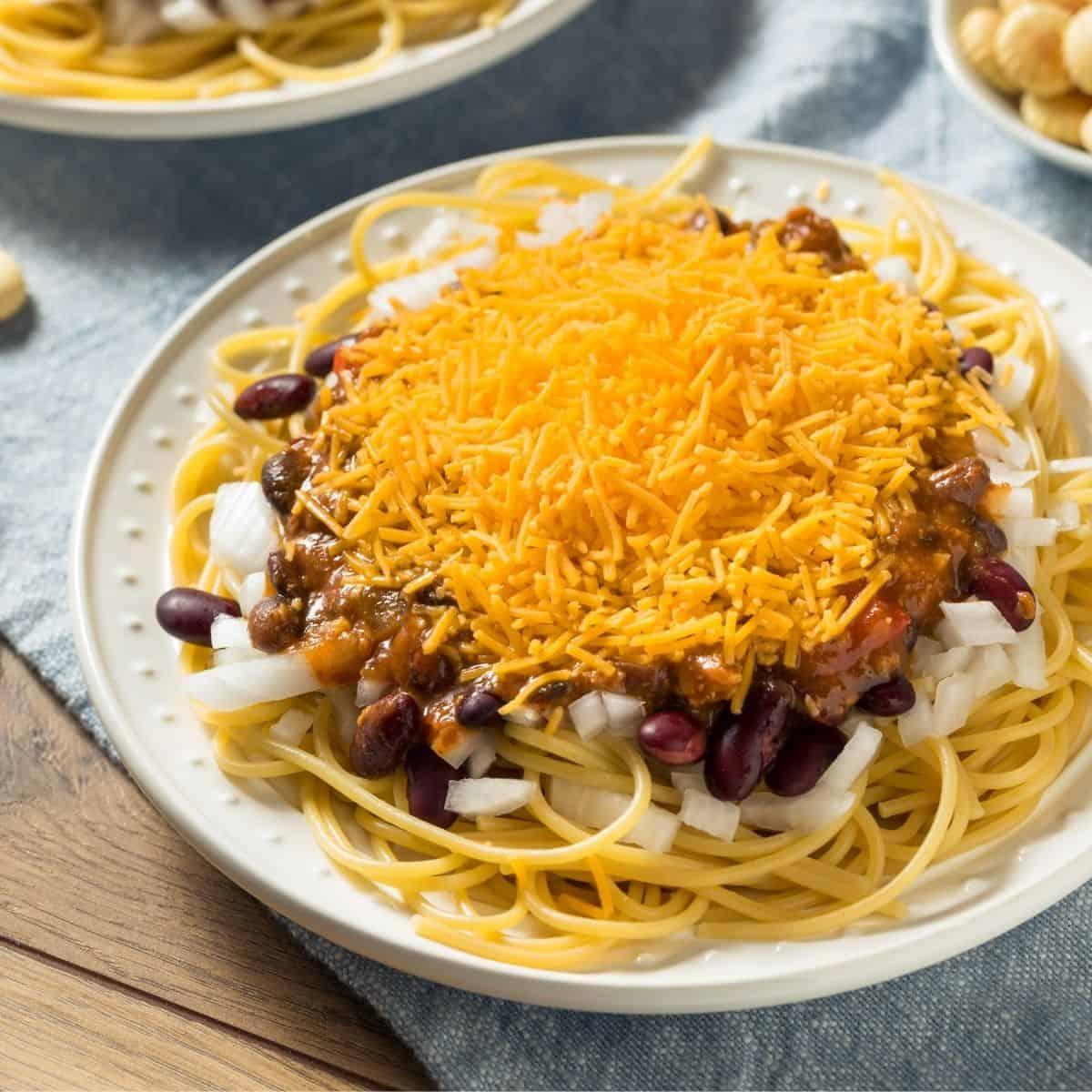bowl of slow cooker cincinnati chili over spaghetti with toppings