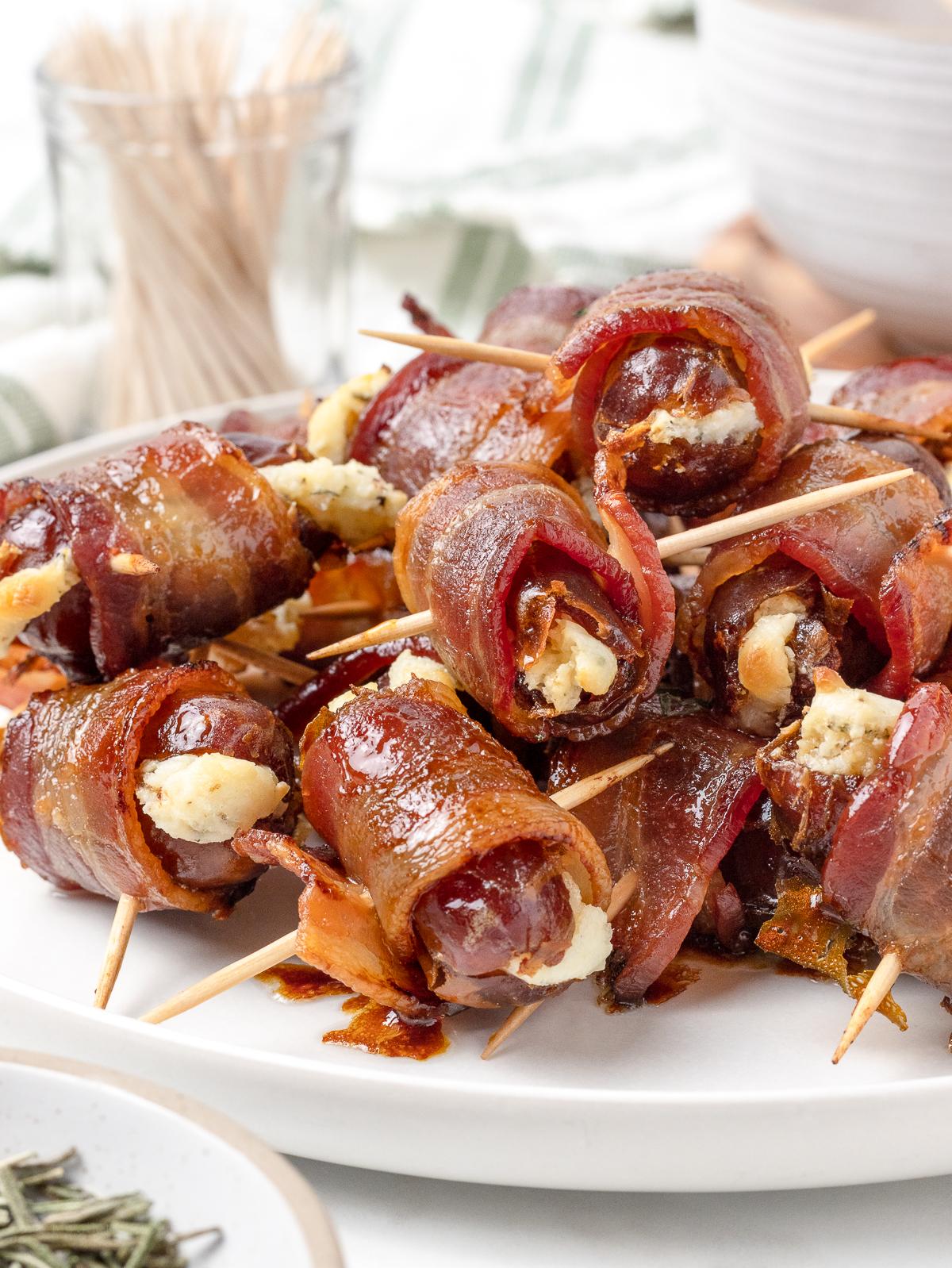 Bacon wrapped dates arepas on a wooden serving board, garnished with fresh herbs