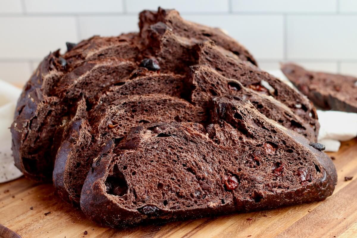 A loaf of chocolate cherry sourdough bread on a wooden cutting board