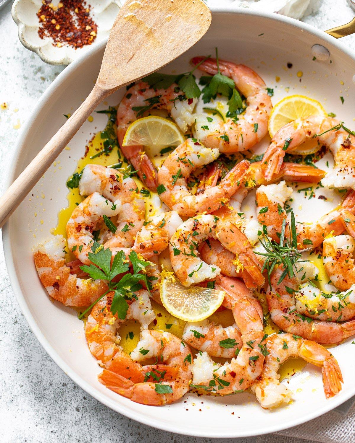 Close-up of a pan with seafood being sautéed, with garlic and herbs
