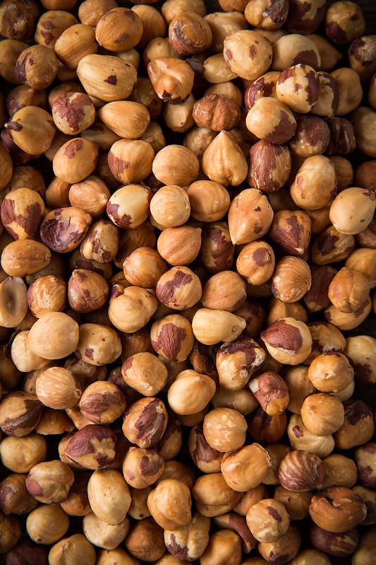 Close-up shot of perfectly toasted hazelnuts with some skins removed, next to a pile of finely ground hazelnuts.