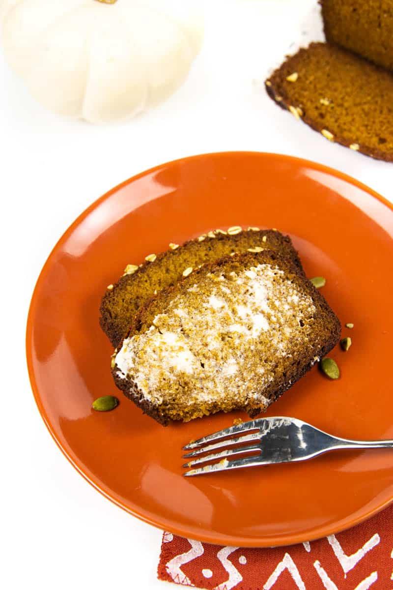 Slice of pumpkin swirl bread on a plate with a fork, next to a steaming cup of coffee