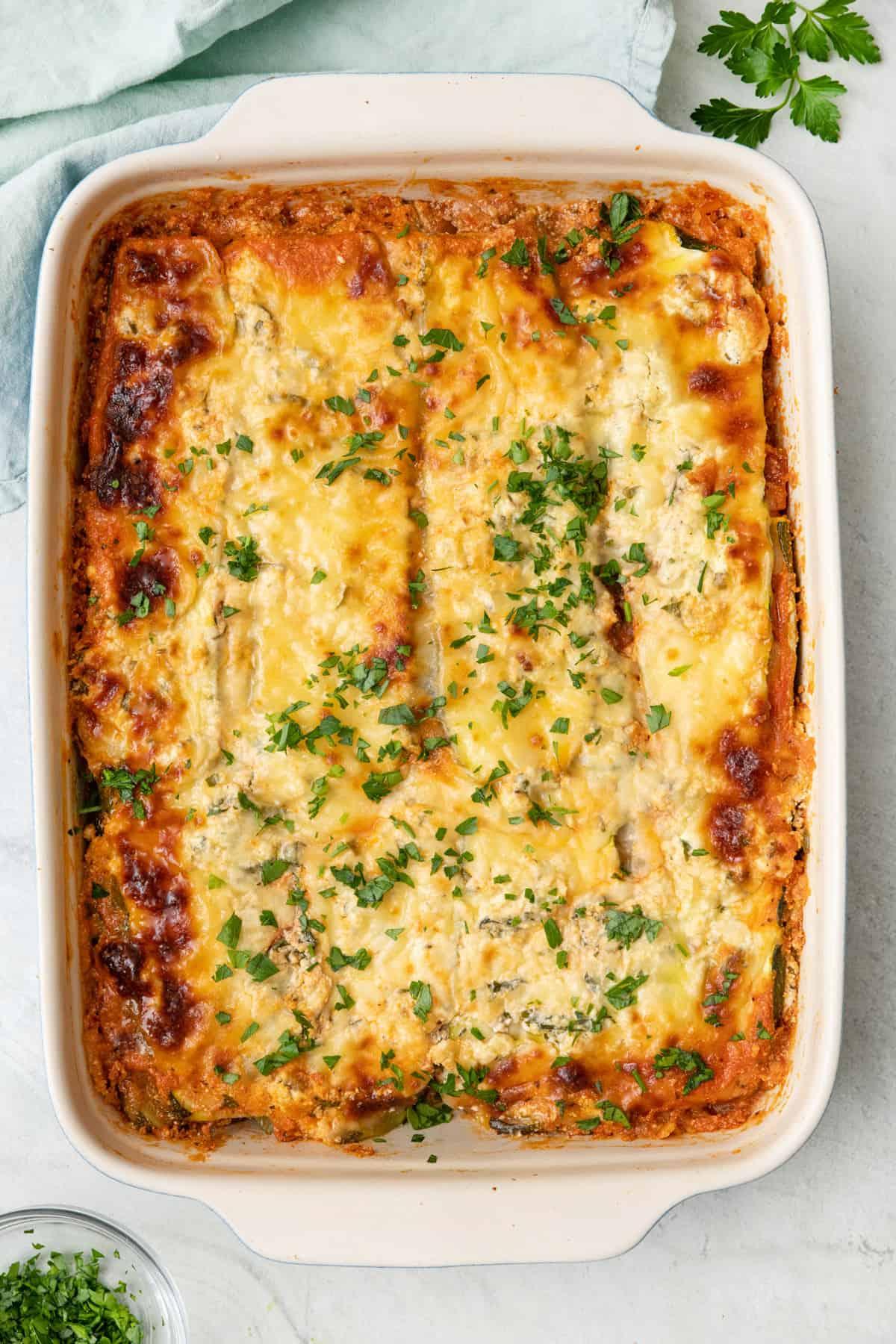 A whole zucchini lasagna served on a plate, garnished with fresh herbs