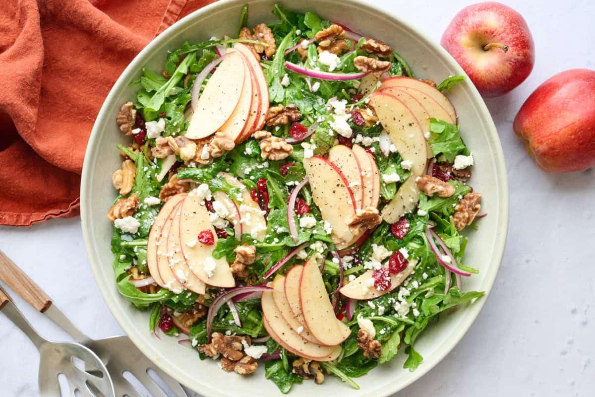 Close-up of apples, walnuts, feta, and arugula being tossed in a salad bowl
