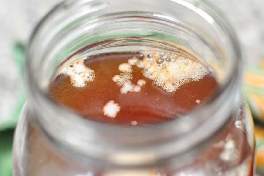 a close-up of the kombucha fermentation process in a glass jar, with visible SCOBY and bubbles