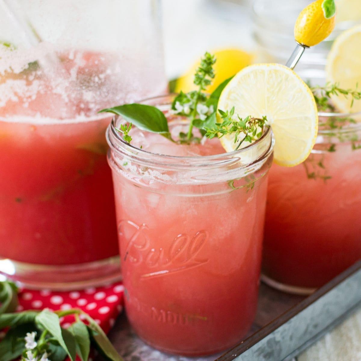 close-up of a glass of watermelon thyme lemonade with ice and a thyme sprig garnish