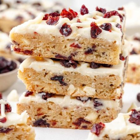 hands slicing a full pan of frosted cranberry bliss bars into squares, showing interior layers