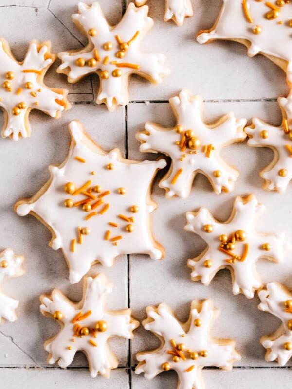A close-up of a hand dipping a snowflake cookie into a bowl of glossy white icing, with other decorated cookies in the background