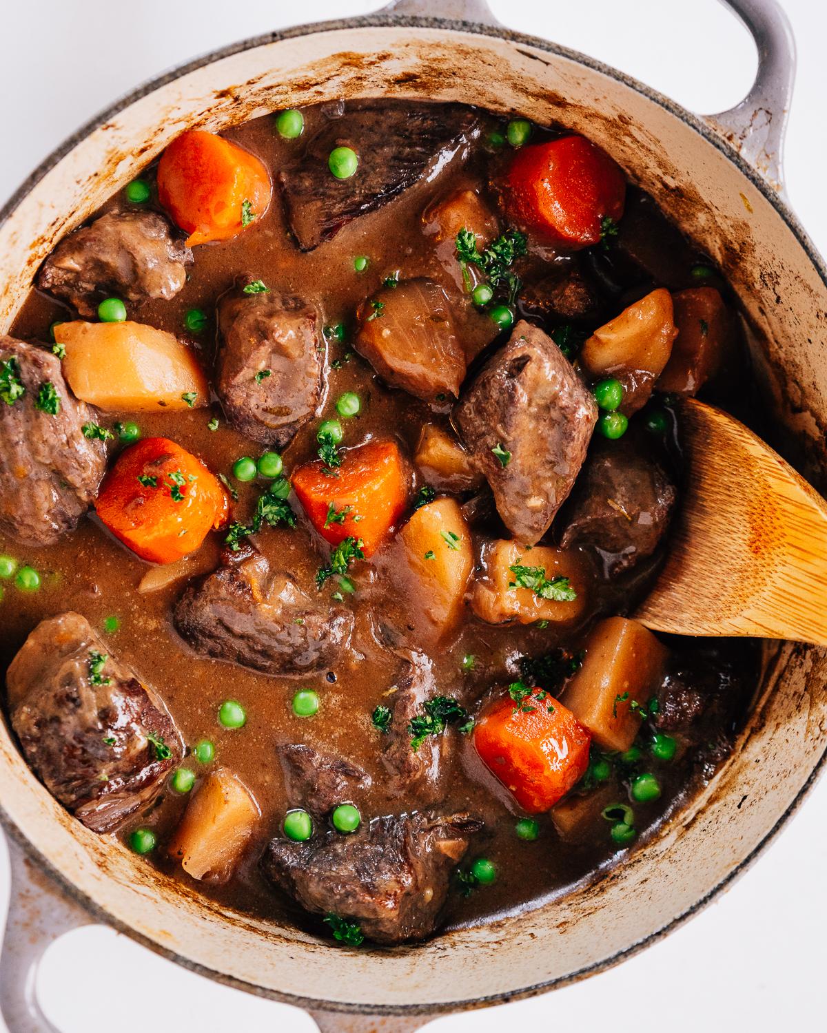 rustic wooden spoon scooping chili garlic beef stew from a dutch oven