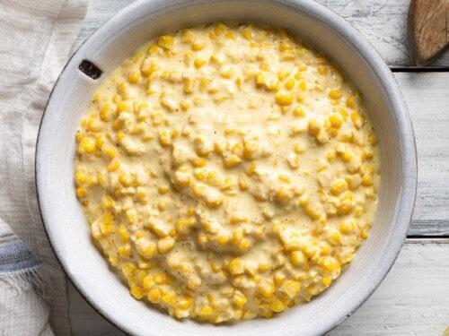 ingredients for creamy corn casserole laid out on a rustic wooden table with fresh corn cobs and a mixing bowl