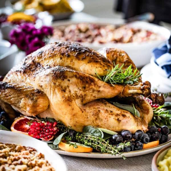 A perfectly golden brown herb roasted turkey with crisp skin, garnished with fresh herbs, on a large serving platter with a holiday table setting