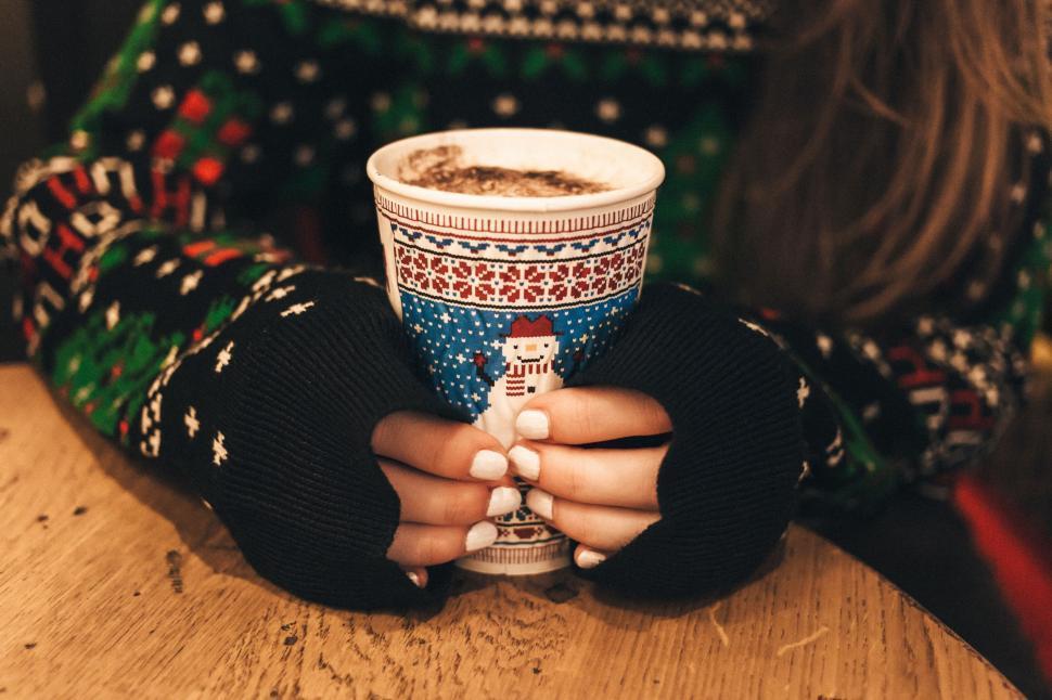 Close-up of hands cupping a warm, steamy mug of dark hot cocoa on a rustic wooden table with a soft, out-of-focus background.