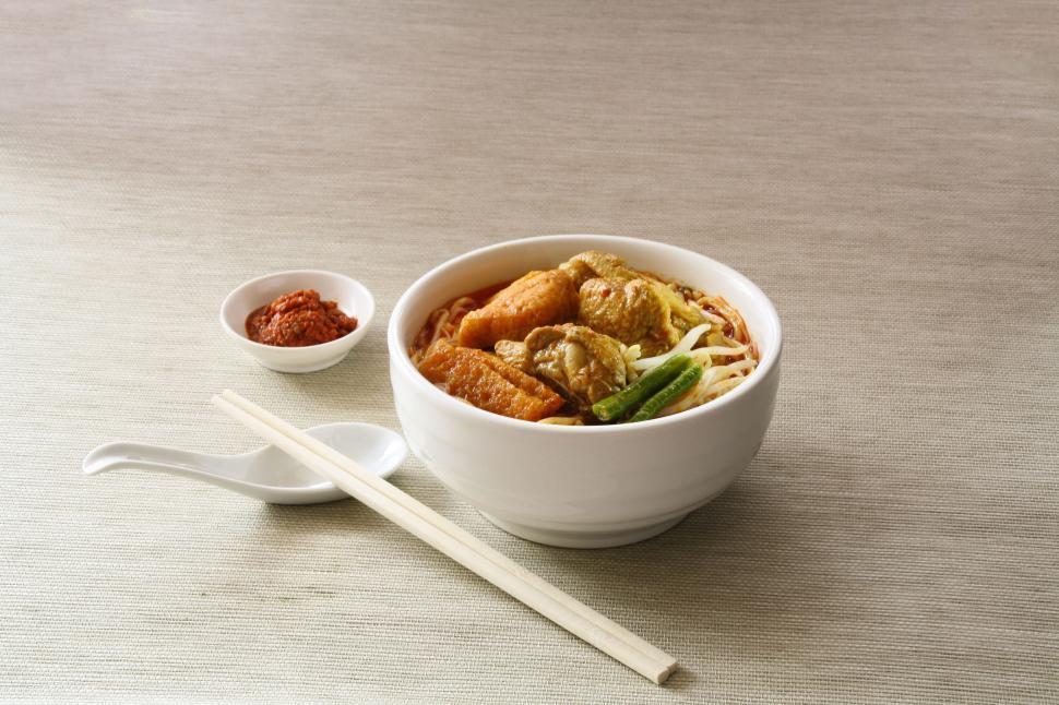 A wide shot of a table setting with a bowl of rice and mushroom chicken and chopsticks