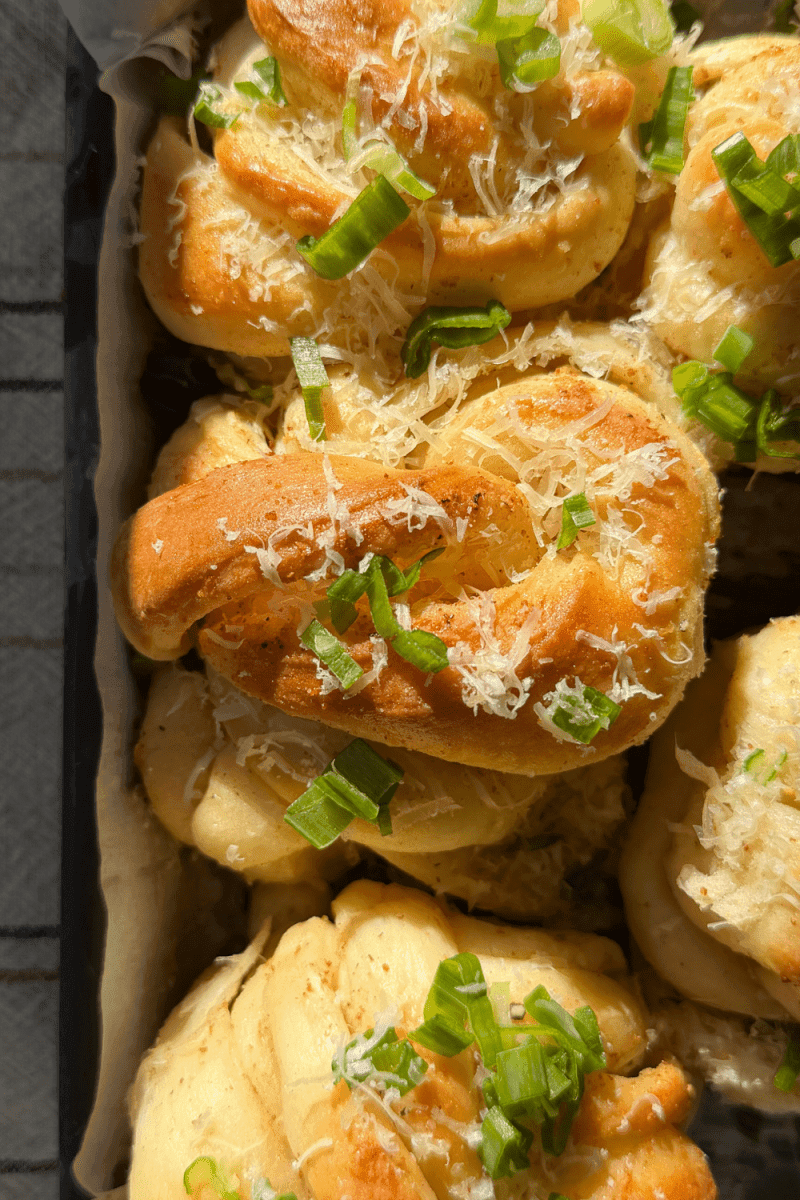 Close-up shot of golden brown garlic knots fresh out of the oven, steam rising slightly, coated in a glistening garlic butter.
