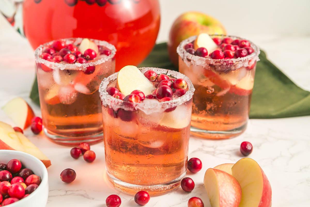Pouring sparkling cider into a punch bowl filled with spiced apple base, garnished with apple slices and cranberries