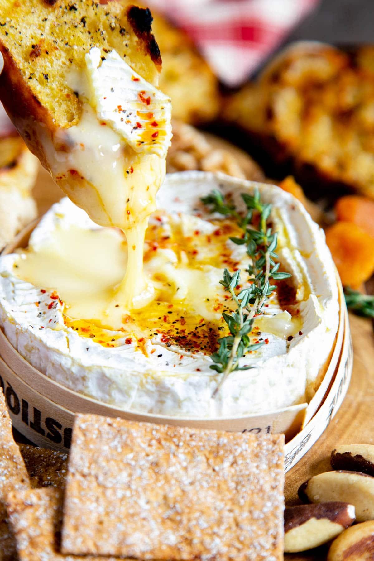 Close-up of baked camembert cheese oozing from its rind, with a piece of baguette dipping into it