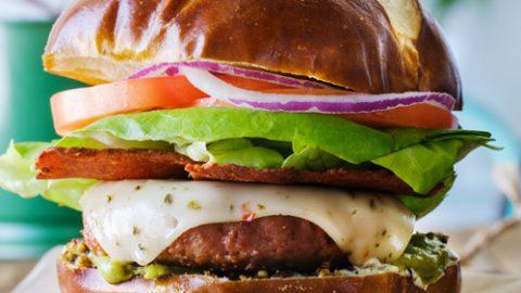 hands assembling a vegan German pretzel burger with pretzel bun, patty, and vegan beer cheese