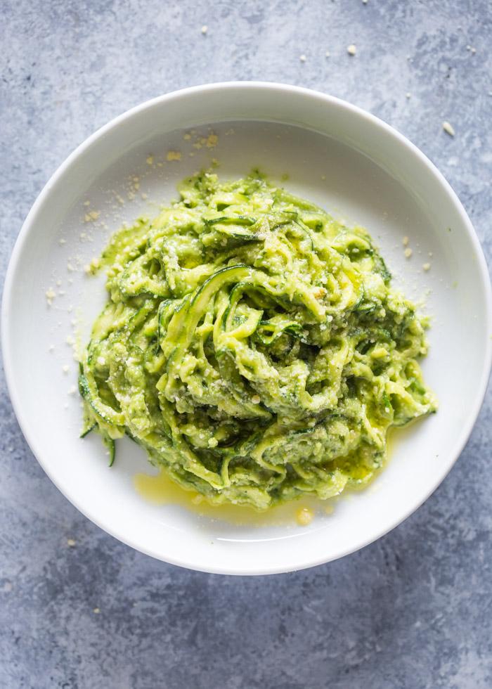 creamy avocado sauce being poured over zucchini noodles