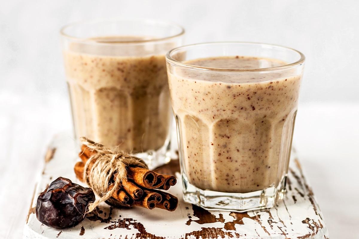 a variety of ingredients for a date almond smoothie, including dates, almonds, almond butter, and cinnamon, arranged on a wooden countertop