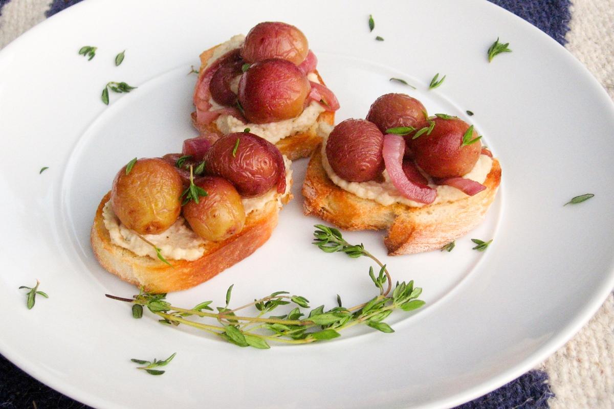 Platter of finished roasted grape crostini with fresh thyme garnish