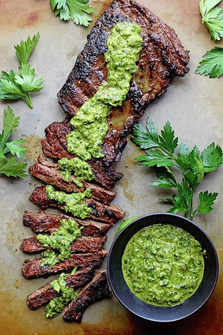 finished smoked brisket being sliced with bright green chimichurri sauce
