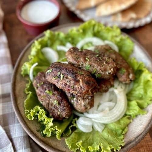a plate of lamb kofta dumplings garnished with cilantro and a side of dipping sauce