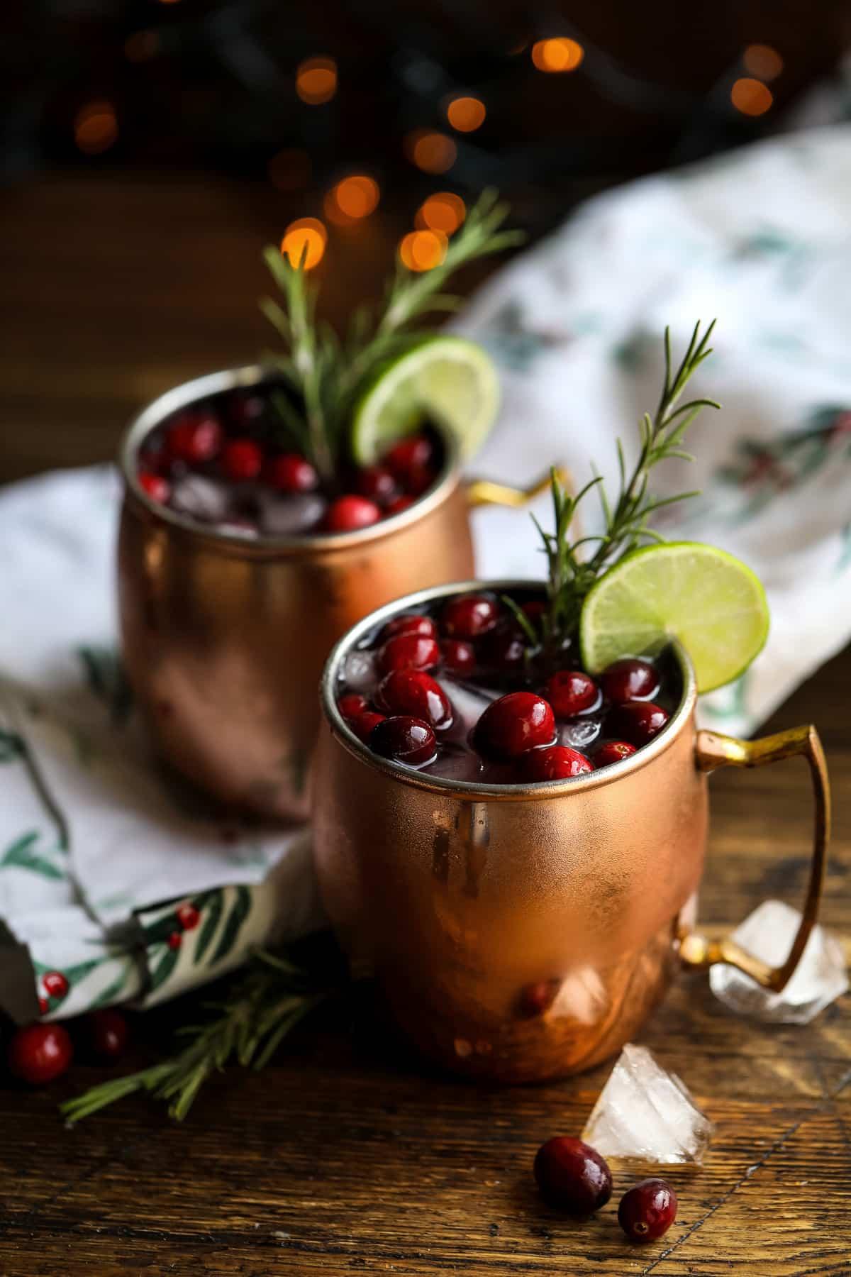 Festive cranberry mule cocktail with frosty lime, fresh cranberries, and rosemary sprig in a copper mug