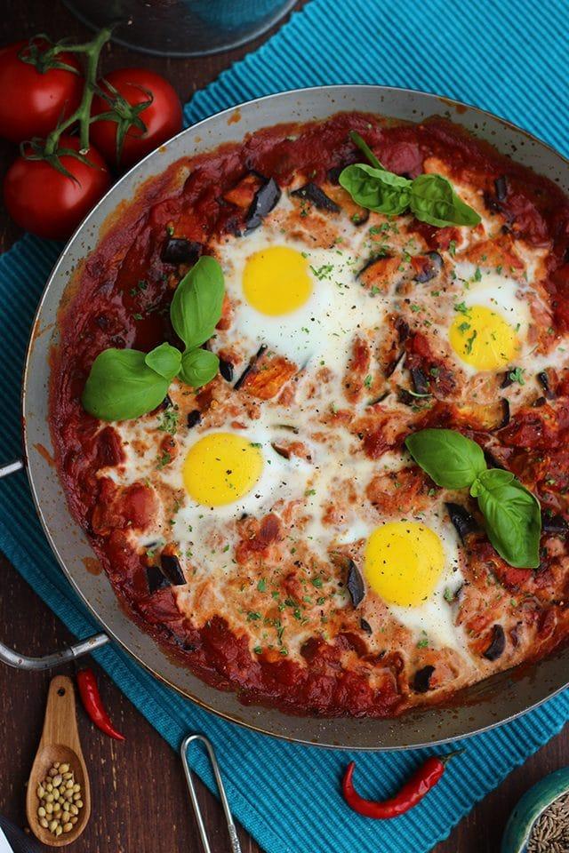 Overhead shot of shakshuka with pepperoni, eggs, and herbs in a skillet