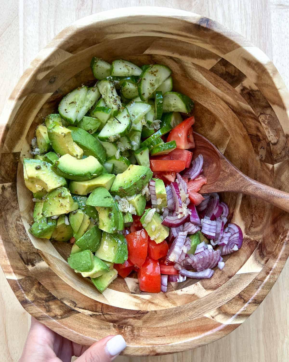 hands mixing avocado, tomato, and onion in a bowl for a keto salad