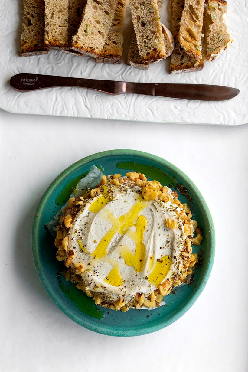 Person spreading cashew cheese on bread and drizzling mint sauce